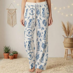 K&ouml;nnte beinhalten: Wei&szlig;e Schlafanzughose mit blauem Hunde- und Blumenmuster. Die Hose hat einen Kordelzug in der Taille und eine lockere Passform. Die Hundeillustrationen sind in einem klassischen Blau-Wei&szlig;-Stil gehalten, der an Porzellan erinnert.