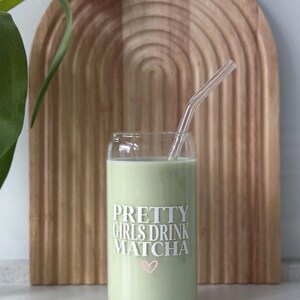 Op de afbeelding: Een glas met een groene drank en een doorzichtige rietje. Het glas heeft de tekst "PRETTY GIRLS DRINK MATCHA" met een roze hart.