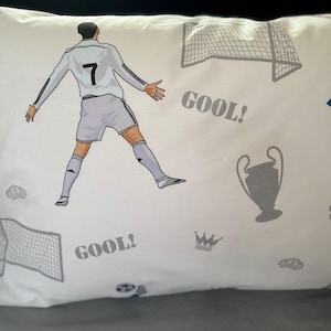 May include: White pillowcase with a soccer player wearing a white jersey with the number 7 on it. The pillowcase has a repeated pattern of soccer goals, crowns, and the word "GOOL!"