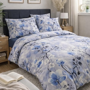 Pode incluir: Um conjunto de roupa de cama com um padrão floral em estilo aguarela azul claro e branco, com ramos azul-escuro e flores semelhantes a orquídeas. O conjunto inclui uma capa de edredão e duas fronhas a condizer com um estampado botânico.