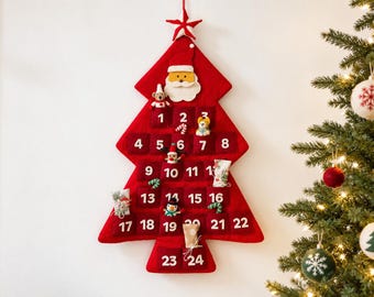 May include: A red felt Christmas tree-shaped advent calendar with twenty-four numbered pockets. The calendar features a white star at the top, a Santa Claus face, and small plush ornaments including a bear, a snowman, and wrapped gift packages.