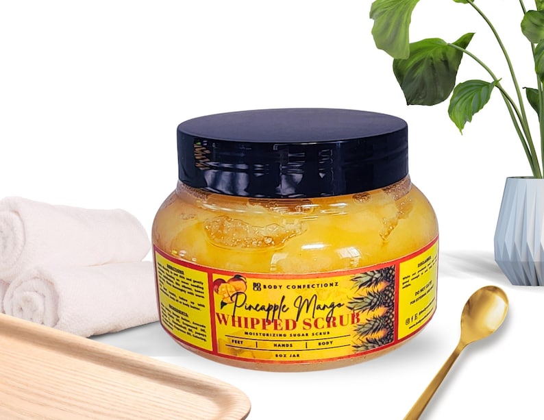 May include: A yellow jar of Pineapple Mango Whipped Scrub, a moisturising sugar scrub for feet, hands, and body. The jar has a black lid and a label with a pineapple and mango design.