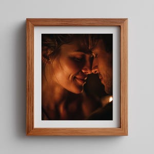 May include: A framed print featuring a tender moment between two people. The image is warm-toned, with soft lighting highlighting their faces as they touch noses. The frame is made of light brown wood, adding a classic touch to the artwork.