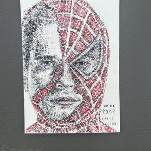 May include: A rectangular print featuring a portrait composed of tiny text. The image shows a face transitioning from a human appearance on the left to a red and black spider-webbed mask on the right. Text in the corner reads MAY 03 2002 KATIE WESTON.