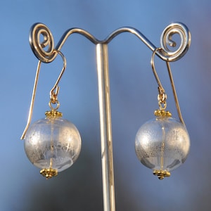 Puede incluir: Un par de pendientes de plata y oro con un diseño redondo de vidrio texturizado. Los pendientes están colgados de un soporte de plata.