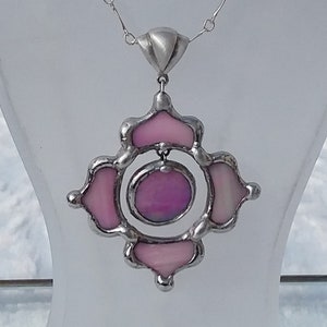 May include: A silver chain necklace with a pink stained glass pendant. The pendant is a circular design with four smaller circles around the center circle. The pendant is made of silver and glass.