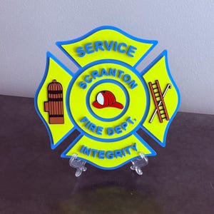 May include: A bright yellow and blue Maltese cross emblem featuring the text SERVICE SCRANTON FIRE DEPT. INTEGRITY. The center displays a red fire helmet, with a brown fire hydrant on the left and a red ladder with a hook on the right side.