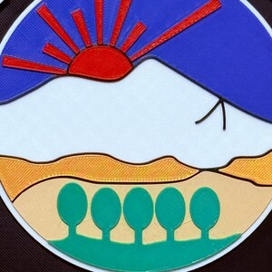 K&ouml;nnte beinhalten: Ein schwarz-wei&szlig;es Polizeibadge mit einer blauen, roten und wei&szlig;en Bergszene mit einer roten Sonne und f&uuml;nf gr&uuml;nen B&auml;umen. Der Text "COLORADO SPRINGS" ist in wei&szlig;en Buchstaben unter der Szene geschrieben.