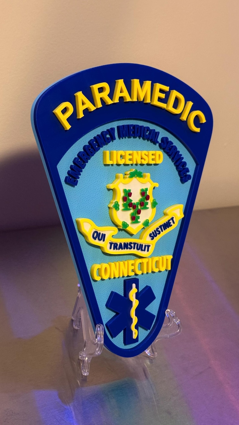 Op de afbeelding: Een blauw en geel Paramedic-bord met de tekst "Emergency Medical Services" en "Licensed". Het bord toont het zegel van de staat Connecticut en een blauw symbool van de levensster.