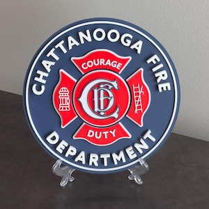 May include: A blue and red round plaque with the words "Chattanooga Fire Department" around the edge. The center features a red cross with a white "C" and "F" inside. The words "Courage" and "Duty" are written on the cross.