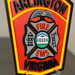 May include: A red, yellow, and black 3D printed sign with the words "ARLINGTON FIRE EMS VIRGINIA" and a stylized eagle and fire department symbol.