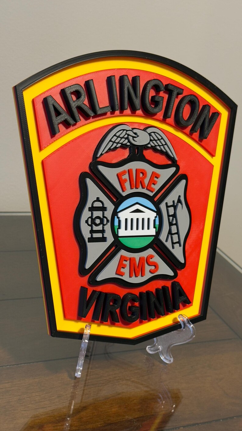 May include: A red, yellow, and black 3D printed sign with the words "ARLINGTON FIRE EMS VIRGINIA" and a stylized eagle and fire department symbol.