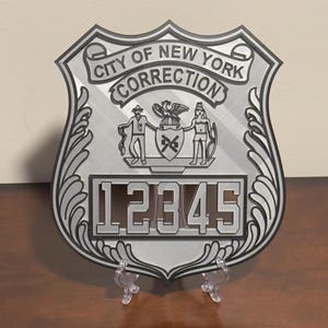 May include: A silver metal badge with the words "City of New York Correction" and the number "12345". The badge features a stylized image of the New York City seal.