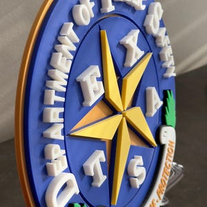 May include: A blue and gold round plaque with the words "Department of Public Safety" and "Texas" in white letters. The plaque features a five-pointed star with a scroll at the bottom that reads "Courtesy - Service - Protection."