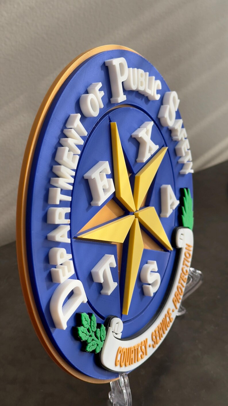 May include: A blue and gold round plaque with the words "Department of Public Safety" and "Texas" in white letters. The plaque features a five-pointed star with a scroll at the bottom that reads "Courtesy - Service - Protection."