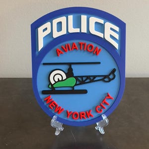 May include: A blue and red plastic sign with the words "POLICE AVIATION NEW YORK CITY" and a cartoon helicopter.