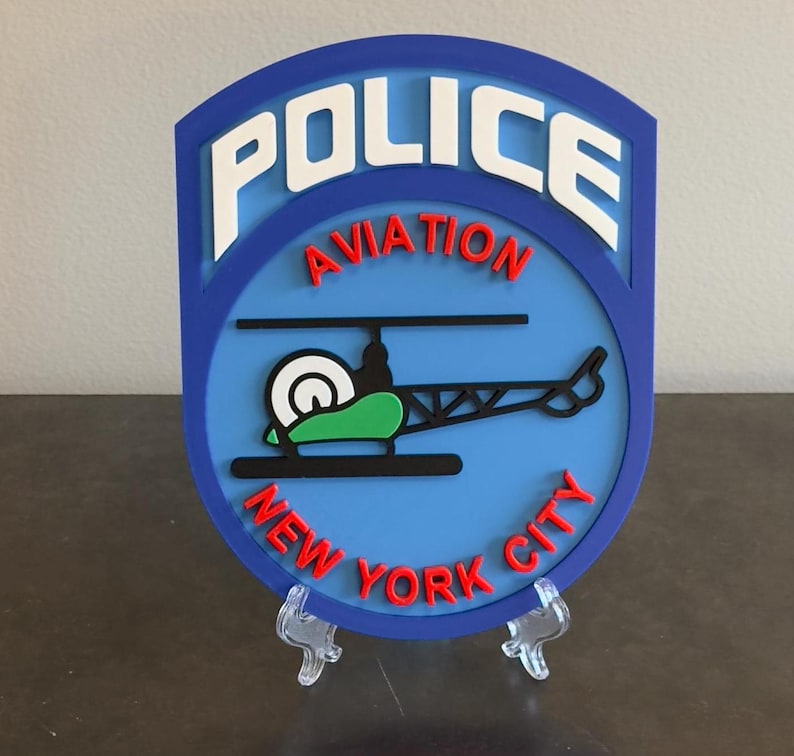 May include: A blue and red plastic sign with the words "POLICE AVIATION NEW YORK CITY" and a cartoon helicopter.
