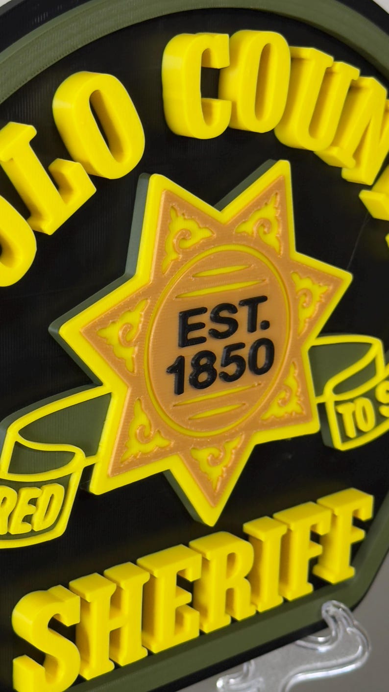 Peut inclure: Panneau jaune et noir avec les mots "LO COUNTY SHERIFF" en lettres en relief. Le panneau pr&eacute;sente une &eacute;toile dor&eacute;e avec le texte "EST. 1850" au centre. Le panneau a une bordure verte.