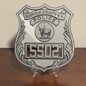 May include: A silver metal police badge with the text "Suffolk County N.Y. Police" and the number "5502". The badge features a stylized bull's head.