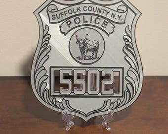 May include: A silver metal police badge with the text "Suffolk County N.Y. Police" and the number "5502". The badge features a stylized bull's head.