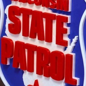 May include: A blue, white, and red sign featuring the words "WISCONSIN STATE PATROL". The sign has a white outline and a red star. The state of Wisconsin is outlined in white.