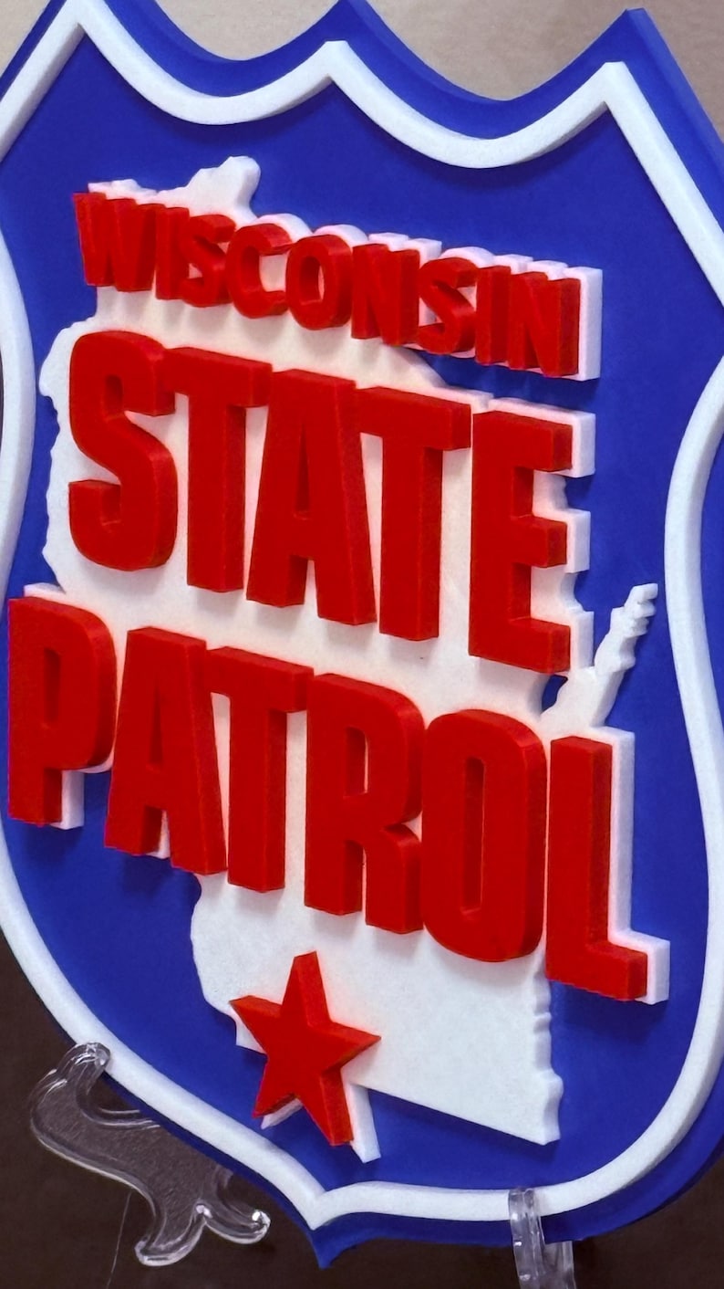 May include: A blue, white, and red sign featuring the words "WISCONSIN STATE PATROL". The sign has a white outline and a red star. The state of Wisconsin is outlined in white.