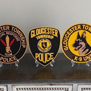 May include: Three Gloucester Township Police Department plaques. The plaques are black, yellow, and brown with the words "Special Response Team Police", "Police", and "K-9 Unit". Each plaque is displayed on a clear stand.