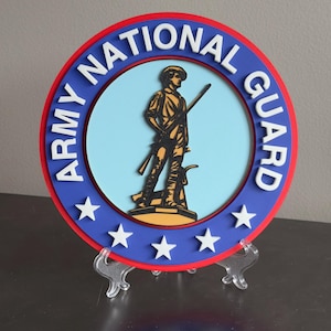 May include: A blue and red circular sign with the words "Army National Guard" in white lettering. The center of the sign features a silhouette of a soldier holding a rifle, standing on a yellow base. There are three white stars around the outer edge of the sign.