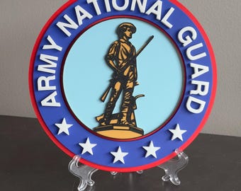 May include: A blue and red circular sign with the words "Army National Guard" in white lettering. The center of the sign features a silhouette of a soldier holding a rifle, standing on a yellow base. There are three white stars around the outer edge of the sign.