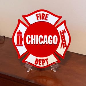May include: A red and white Chicago Fire Department emblem. The emblem is in the shape of a Maltese cross, with the words "FIRE" and "DEPT" in white. The word "CHICAGO" is in white in the center.