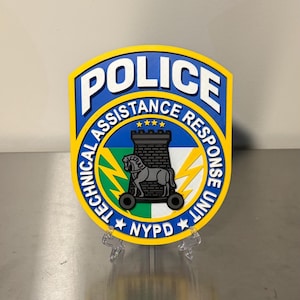 May include: A shield-shaped emblem with the words "POLICE" and "ASSISTANCE RESPONSE UNIT" in white lettering on a blue background. The emblem features a central design of a castle and horse, with the text "NYPD" at the bottom.