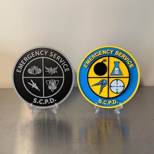 May include: Two circular plaques labeled EMERGENCY SERVICE S.C.P.D. The left plaque is black with white icons including a gas mask and bomb. The right plaque is blue and yellow with icons of a bomb, a chemical flask with a skull, a tool, and a target.