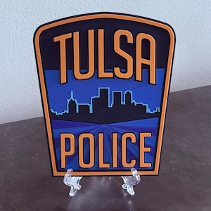 May include: A blue and orange Tulsa Police Department patch with a skyline silhouette and the words "TULSA POLICE" in orange.