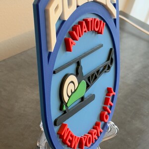 May include: A blue and white 3D printed police badge with the words "POLICE AVIATION NEW YORK CITY" and a helicopter graphic.