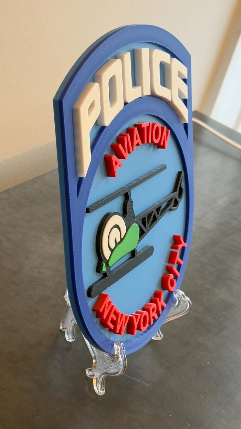 May include: A blue and white 3D printed police badge with the words "POLICE AVIATION NEW YORK CITY" and a helicopter graphic.