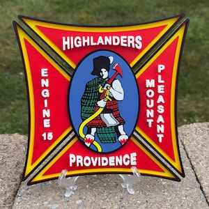 May include: A square, red and yellow emblem with the words "Highlanders", "Engine 15", "Mount Pleasant", and "Providence" in white. The emblem features a cartoon figure in a kilt holding a fire axe and hose.
