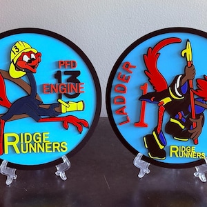 May include: Two round, black-framed plaques with a blue background and a cartoon roadrunner wearing a firefighter's helmet. The left plaque reads "PFD 13 ENGINE" and the right plaque reads "LADDER 1". Both plaques have the text "RIDGE RUNNERS" at the bottom.