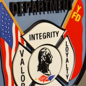 Op de afbeelding: Een 3D-geprint embleem voor de brandweer van Yonkers. Het ontwerp bevat de tekst "YONKERS FIRE DEPARTMENT", een Amerikaanse vlag, een rode vlag en de woorden "INTEGRITY", "VALOR", "LOYALTY" en "DEDICATION".