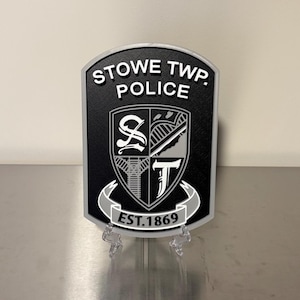 May include: A black and silver Stowe Twp. Police badge with the text "STOWE TWP. POLICE" at the top and "EST.1869" at the bottom. The badge features a shield design with a stylized emblem in the center.