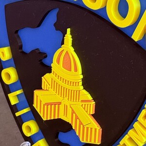 May include: A badge with the words "MADISON POLICE DEPARTMENT" in yellow, and a yellow and orange building design on a black background, set against a blue backdrop. The badge is shield-shaped.