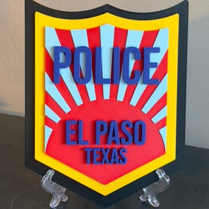May include: A red, yellow, and blue police badge with the text "POLICE", "EL PASO", and "TEXAS".