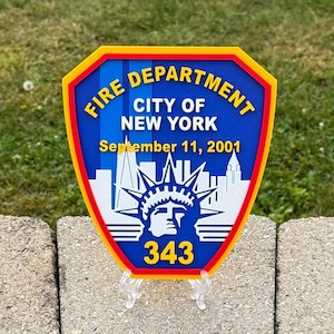 May include: A shield-shaped emblem with the text "Fire Department City of New York" in yellow and blue. The emblem commemorates September 11, 2001, and features the Statue of Liberty and the number 343.