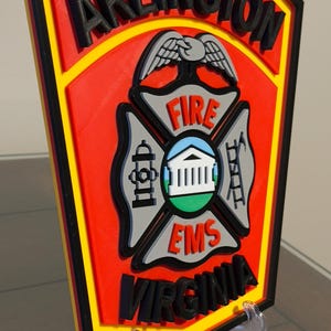 May include: A red, yellow, and black 3D printed sign with the words "ARLINGTON FIRE EMS VIRGINIA" and a stylized eagle and fire department symbol.