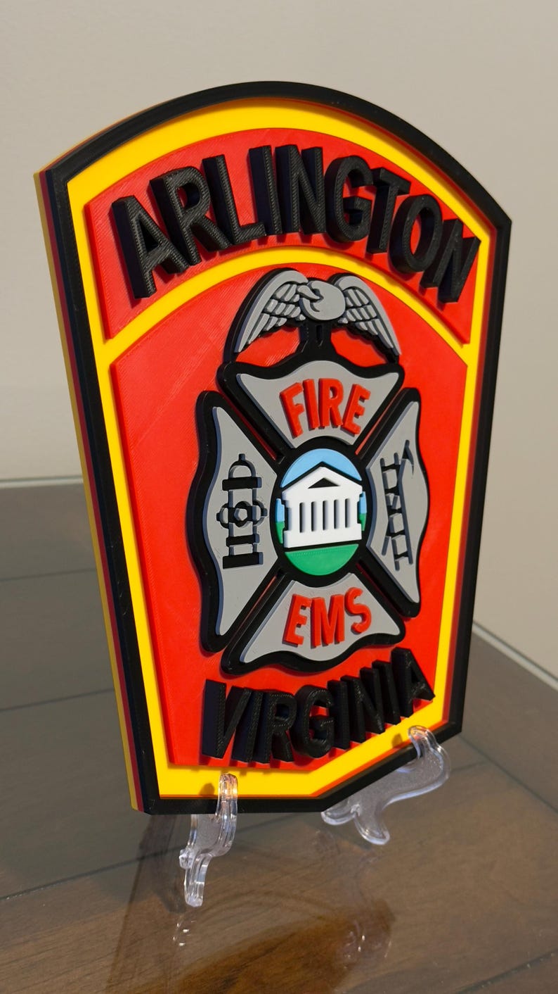 May include: A red, yellow, and black 3D printed sign with the words "ARLINGTON FIRE EMS VIRGINIA" and a stylized eagle and fire department symbol.