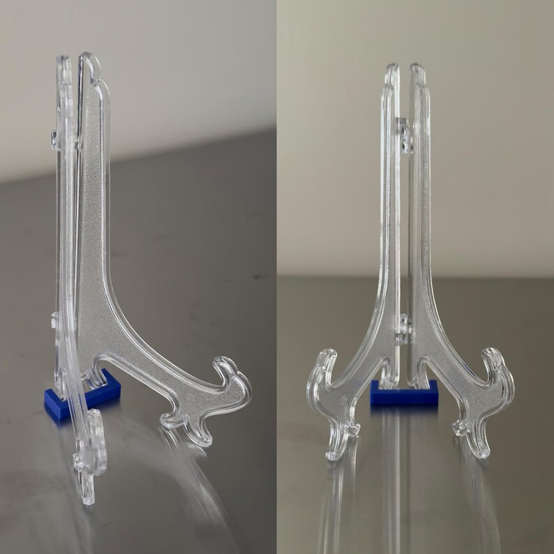May include: Clear acrylic display stands with a decorative scroll design and blue bases. These stands are designed to hold plates, artwork, or other items. The stands are shown from the side and front.
