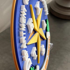 May include: A blue and yellow 3D printed wall plaque with the words "Department of Public Safety" and a star with the letters "E-9-1-1" around it. The plaque is on a clear plastic stand.