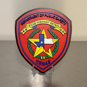May include: A red, blue, and yellow Texas Highway Patrol emblem. The emblem features the words "DEPARTMENT OF PUBLIC SAFETY" and "TEXAS HIGHWAY PATROL" in blue. The Texas state outline is in blue, white, and yellow, with a star in the center.