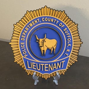 May include: A gold and blue police badge with a black outline. The badge features a bull's head and the text "Police Department, County of Suffolk, N.Y. Lieutenant".