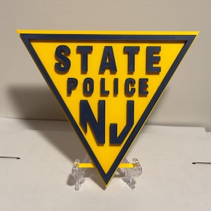 May include: A yellow triangular sign with a black border. The sign says "STATE POLICE NJ" in blue letters.