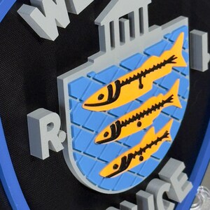 May include: A 3D sign featuring the words "WESTERLY POLICE" in gray block letters. The sign has a black background with a blue border. The center design includes a blue shield with three yellow fish.